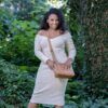 A woman in a beige off-shoulder dress stands outdoors, smiling at the camera while holding the Kinsley Concealed Carry Crossbody Gun Handbag with RFID Slim Wallet (Faux Leather).